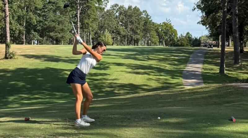 A golfer prepares to tee off on a tree-lined course.